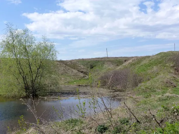 木の生えていない丘の低地の小さな池 中間の平野 春池と丘陵の風景 — ストック写真