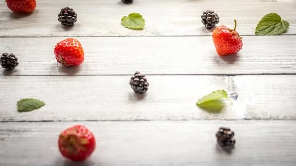 Creative blackberry, Strawberries and leaves colorful pattern on white wooden background. Flat lay. Food concept.