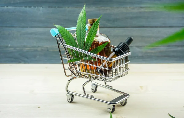 Wózek supermarket z liści marihuany i medycyny konopnej CBD olej na drewnianym tle — Zdjęcie stockowe