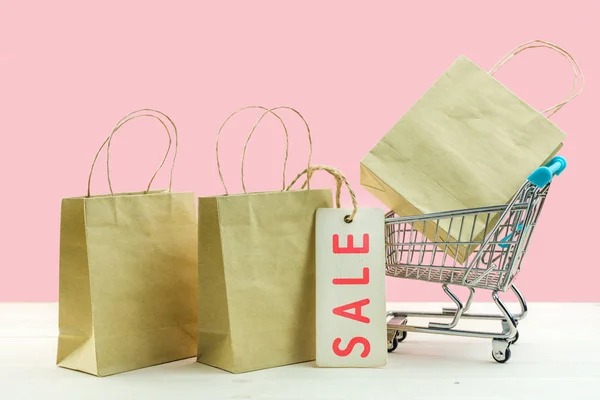 Trolley kar en papieren boodschappentassen op roze achtergrond. Creatief idee voor online winkelen, zomer Sale, supermarkt, korting promotie — Stockfoto