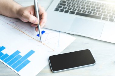 Finansal kağıt grafikler ve dizüstü bilgisayar ile çalışan elinde kalem tutan adam