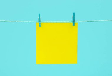Mavi arkaplana karşı mandallı sicim üzerinde sarı boş kağıt levha
