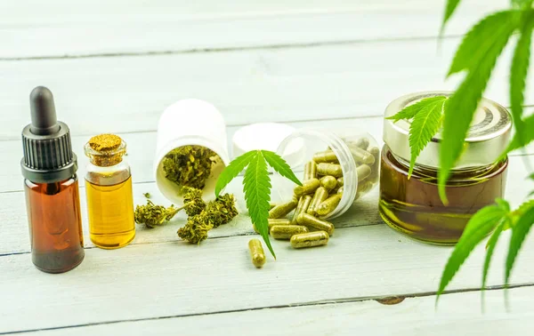 CBD Cannabidiol olie glazen flessen, pillen bloemknoppen en cannabis Leafs op heldere houten achtergrond — Stockfoto