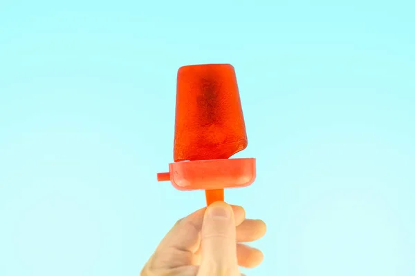 Hand holding red Frozen Popsicle Ice Pop against Summer Blue Sky