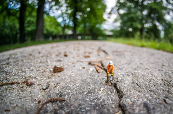 Operaio edile in miniatura con martello su crepa in asfalto — Foto Stock