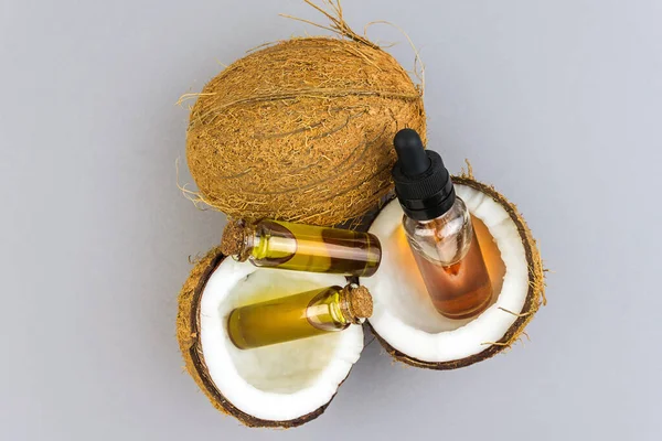 Vue du dessus des noix de coco demi-coupées aux huiles essentielles de noix de coco en bouteilles de verre isolées sur gris clair — Photo