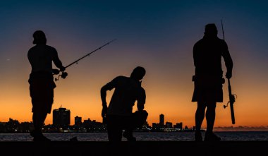Havana, Küba, 19 Kasım 2017 - Gölgede üç adam gün batımında Malecon 'da balık tutarken görüldü