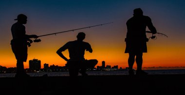 Havana, Küba, 19 Kasım 2017 - Gölgede üç adam gün batımında Malecon 'da balık tutarken görüldü
