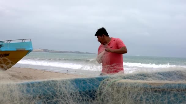 San Pedro, Ecuador - 20180915 - Vista bassa dell'uomo in piedi sulla spiaggia accanto alla barca e alla rete di riparazione . — Video Stock