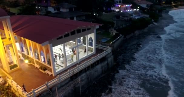 La Entrada, Ecuador - 20180914 - Drone Aerial Time Lapse - Drone Pans Across Glass Fronted Church with People Inside at Night at High Tide . — стоковое видео