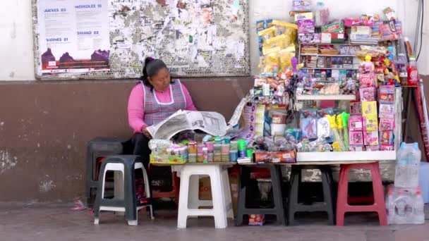 Cuenca, Ecuador - 20180920 - La mujer se sienta junto a su mesa de productos para vender, leyendo el periódico . — Vídeos de Stock