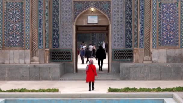 Керман, Иран - 2019-04-06 - Женщина в красном входит в мечеть Ганджали, пока дети играют на заднем плане — стоковое видео