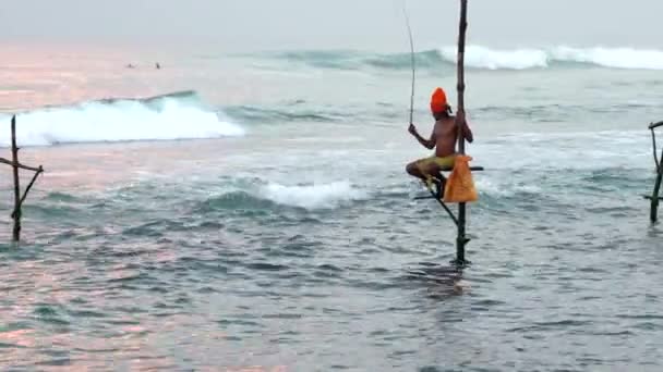 Galle, Sri Lanka - 2019-04-01 - Stilt Fishermen - One Fisher With Surfers in Background — Stock Video