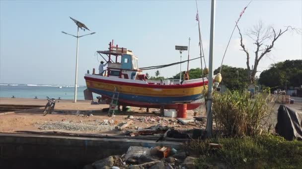 Galle, Sri Lanka - 2019-04-01 - Dois homens trabalham em barcos pequenos atracados a seco na praia - Side — Vídeo de Stock