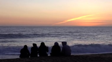 Vina del Mar, Şili - 2019-07-18 - Beş arkadaş sahilde oturur ve dalgalı dalgaların önünde güneşin batışını izlerler