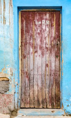 Kırık alçılı mavi tuğla duvardaki solmuş kırmızı kapı.