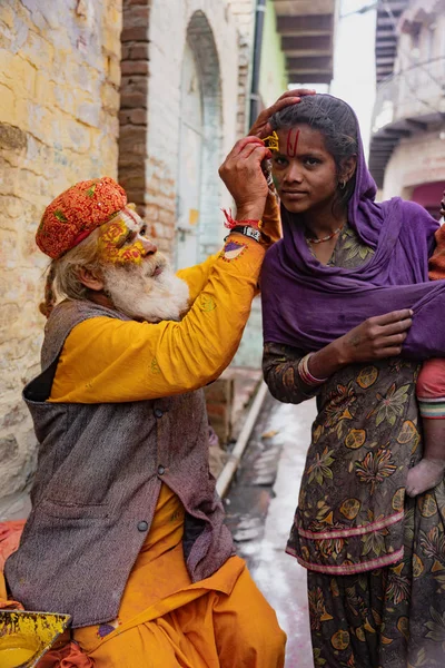 Starší muž maluje symboly pomocí zlaté malby na čelo ženy — Stock fotografie