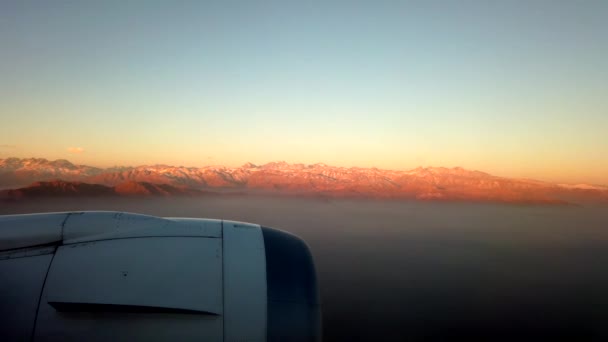 Vliegtuig venster-wolken hieronder met zonsondergang Moutains in afstand — Stockvideo