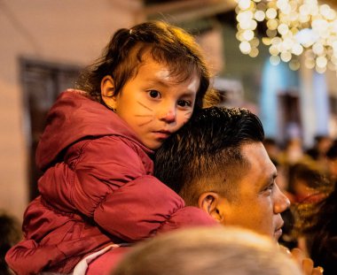 Cuenca, Ekvador - 2019-12-31 - Festivalde boyalı kedi beceren çocuklar babalarının omuzlarına biniyor