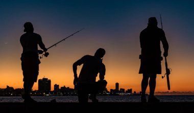 Üç adam gün batımında iskelede balık tutarken görüldü.