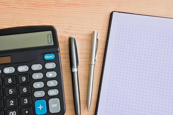 Rekenmachine, twee balpennen en een notitieblok op een houten tafel. Copyspace — Stockfoto