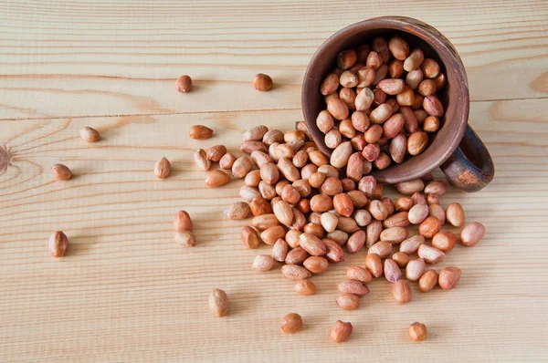 Las nueces de cacahuete se dispersan de una taza en una mesa de madera — Foto de Stock