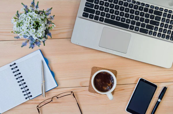 Laptop, notepad with pen, cup of coffee, smartphone, glasses and