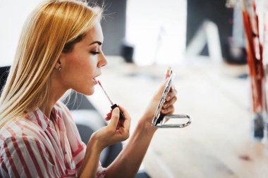 Genç ve güzel bir kadın aynanın yanında makyaj yapıyor.