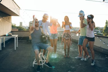 Bir grup mutlu genç arkadaş çatıda parti veriyor.