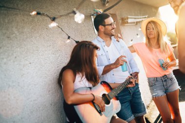 Bir grup mutlu genç arkadaş çatıda parti veriyor.