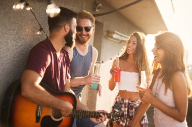 Bir grup mutlu genç arkadaş çatıda parti veriyor.