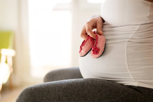 妊娠中の女性は赤ちゃんの女の子の靴を彼女の腹につかまって — ストック写真