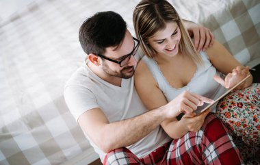Genç mutlu çift yatak odasında dijital tablet kullanma