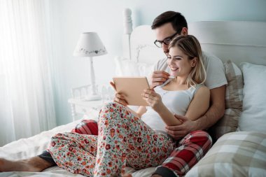 Genç mutlu çift yatak odasında dijital tablet kullanma