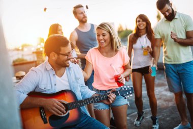 Bir grup mutlu genç arkadaş çatıda parti veriyor.