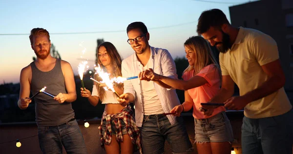Friends enjoying a rooftop party and dancing with sparklers in hands