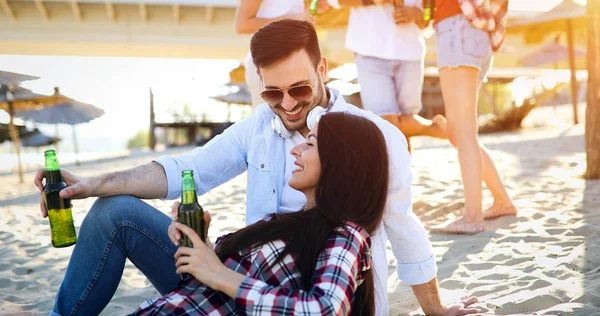 幸せな若いカップル笑顔とビーチでビールを飲む — ストック写真