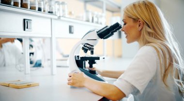 Laboratuvarda mikroskoptan bakan genç kadın bilim adamı.