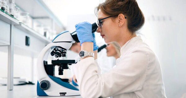Молодая женщина-ученый смотрит в микроскоп в лаборатории