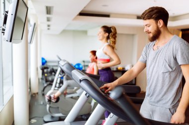 Kardiyo egzersiz yaparken spor salonunda koşu bandı üzerinde çalışan insanlar