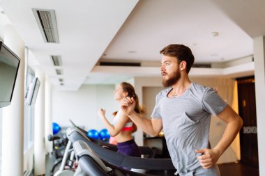 Kardiyo egzersiz yaparken spor salonunda koşu bandı üzerinde çalışan insanlar