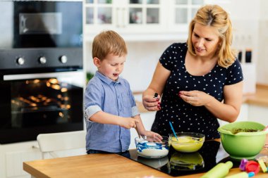 Çocuk modern mutfakta annesine kurabiye yapması için yardım ediyor.