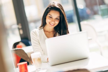 Güzel genç şirin esmer kafede dizüstü bilgisayar kullanarak