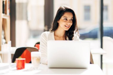 Güzel genç şirin esmer kafede dizüstü bilgisayar kullanarak