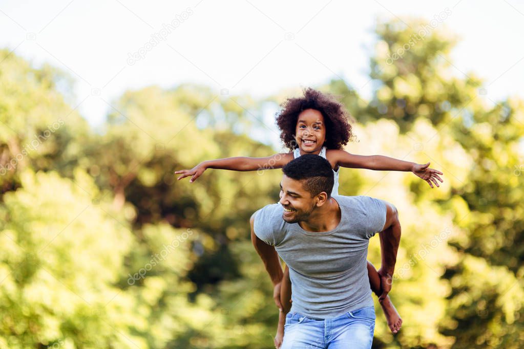 Portrait of young father carrying his daughter on his back in nature