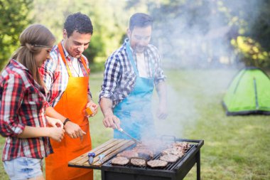 Mutlu insanlar kamp yapıyor ve dışarıda bbq partisi veriyor.