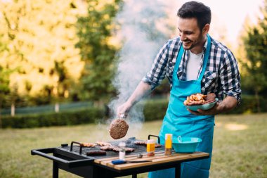 Handsome young man preparing barbecue for friends clipart