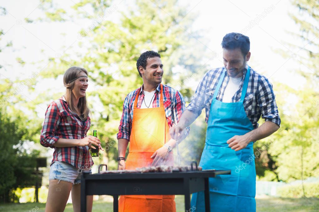 Young happy people enjoying barbecuing in forest