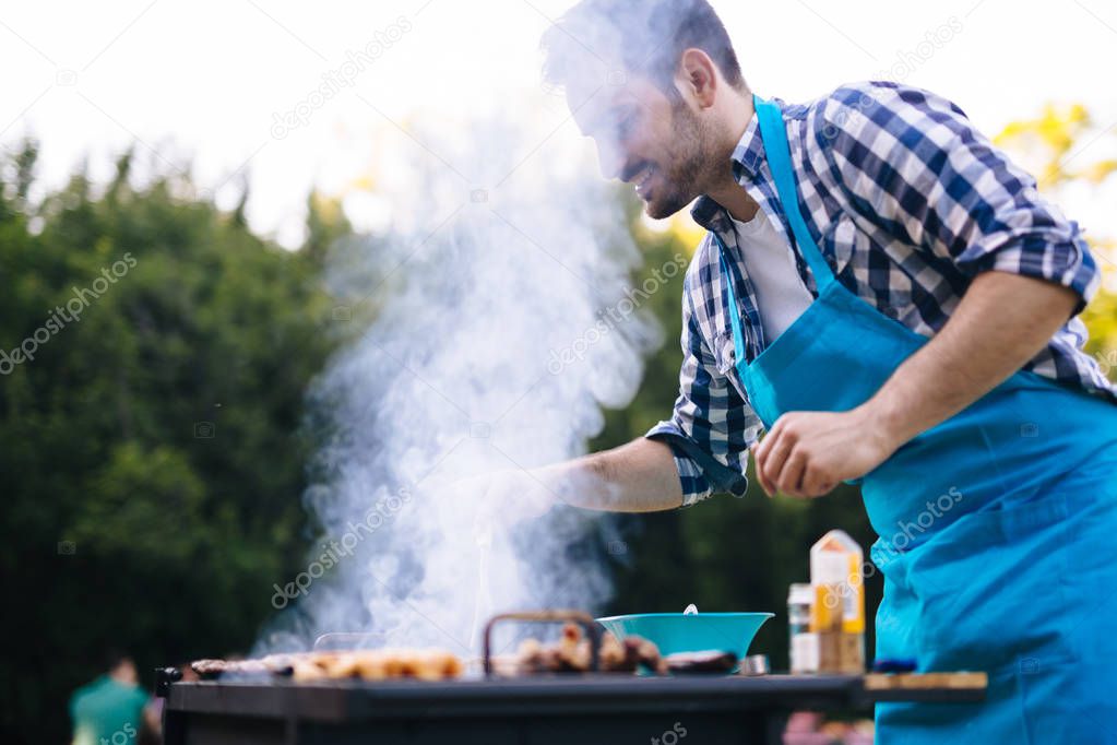 Handsome happy male preparing barbecue outdoors for friends