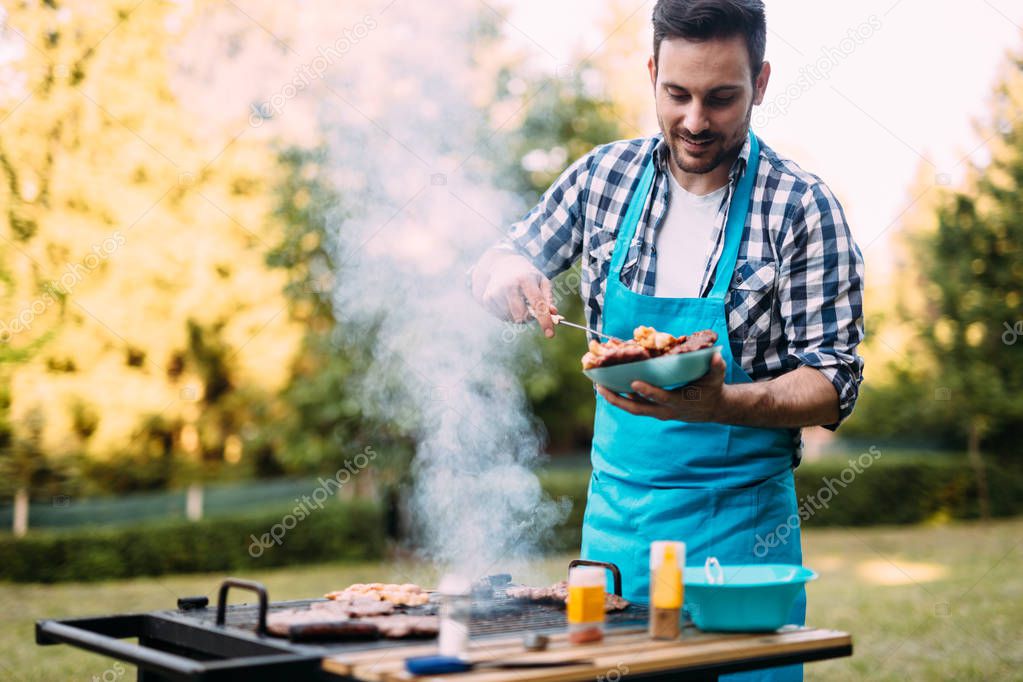 Handsome happy male preparing barbecue outdoors for friends